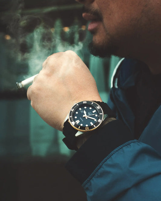 A black dial watch with a gold-toned bezel and case, featuring white hour markers and hands, worn on a wrist.