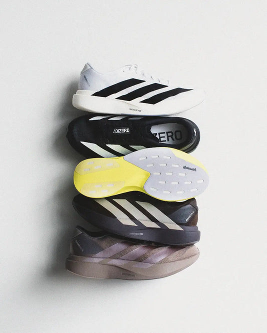 Stacked adidas adizero running shoes in white, black, and gray with signature three stripes.