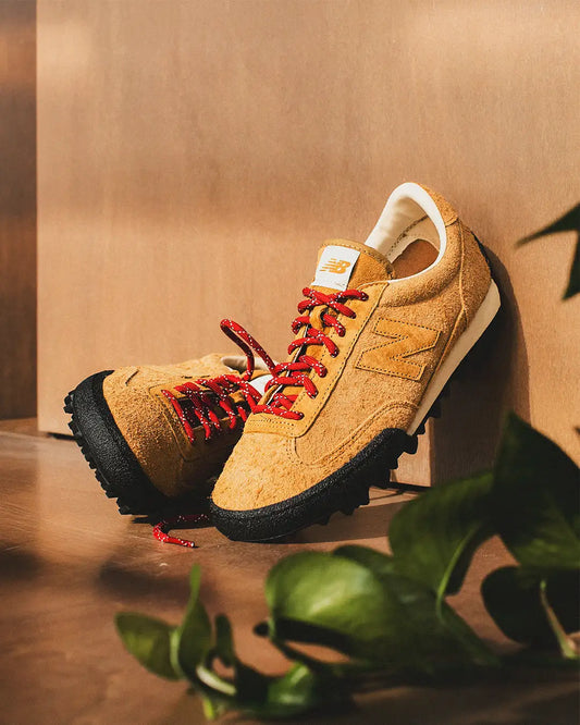 Tan suede new balance sneaker with red laces and black rubber sole.